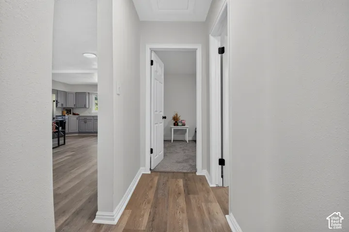 Hallway featuring wood-finish flooring, white paneled doors, matte black hardware, and neutral wall tones