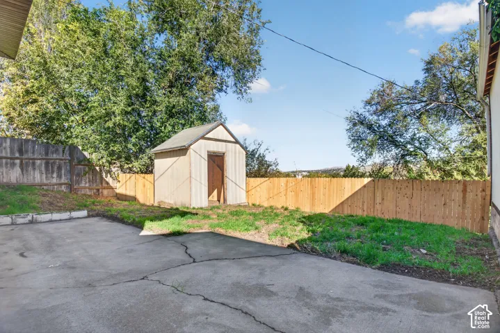 Rear exterior grounds featuring a concrete pad, detached wood-frame storage shed, and perimeter wood fencing
