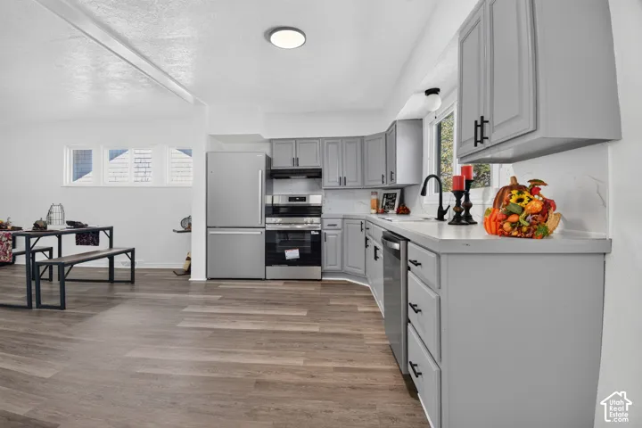 Kitchen featuring grey shaker-style cabinetry, stainless steel appliances, matte black hardware, stone-surface countertops, and wood-finish flooring