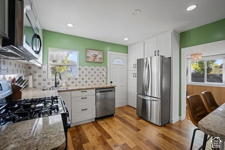 Kitchen featuring wood-finish flooring, white cabinetry, stainless steel appliances, patterned tile backsplash, and recessed ceiling lighting