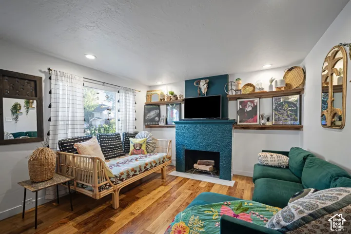 Interior featuring a blue-textured fireplace surround, wood-finish flooring, built-in wooden wall shelving, recessed ceiling lighting, and a multi-pane window