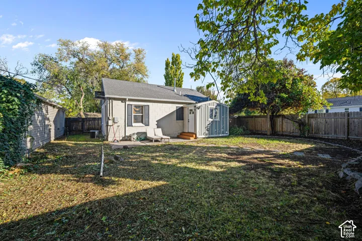 Fenced backyard featuring mature trees, a concrete patio, and a detached exterior structure