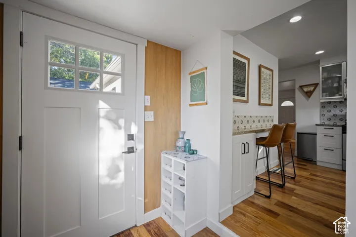 Entryway featuring a white door with a six-pane window, wood-finish flooring, natural wood-tone wall paneling, and a built-in kitchen peninsula with white shaker-style cabinetry