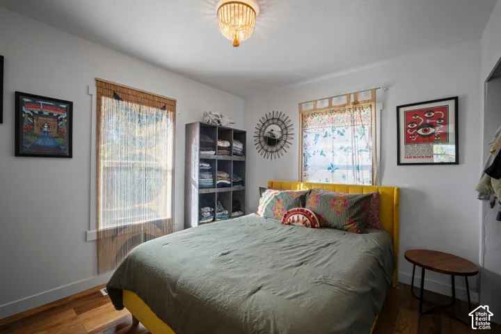 Bedroom featuring wood-finish flooring, dual windows, and a flush-mount crystal-style beaded light fixture