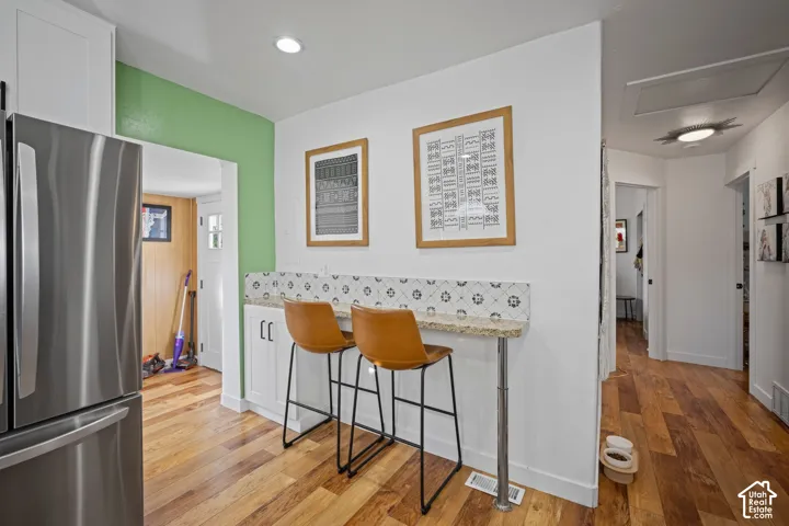Kitchen breakfast bar featuring white cabinetry, stone-finish countertop, patterned tile backsplash, and wood-finish flooring