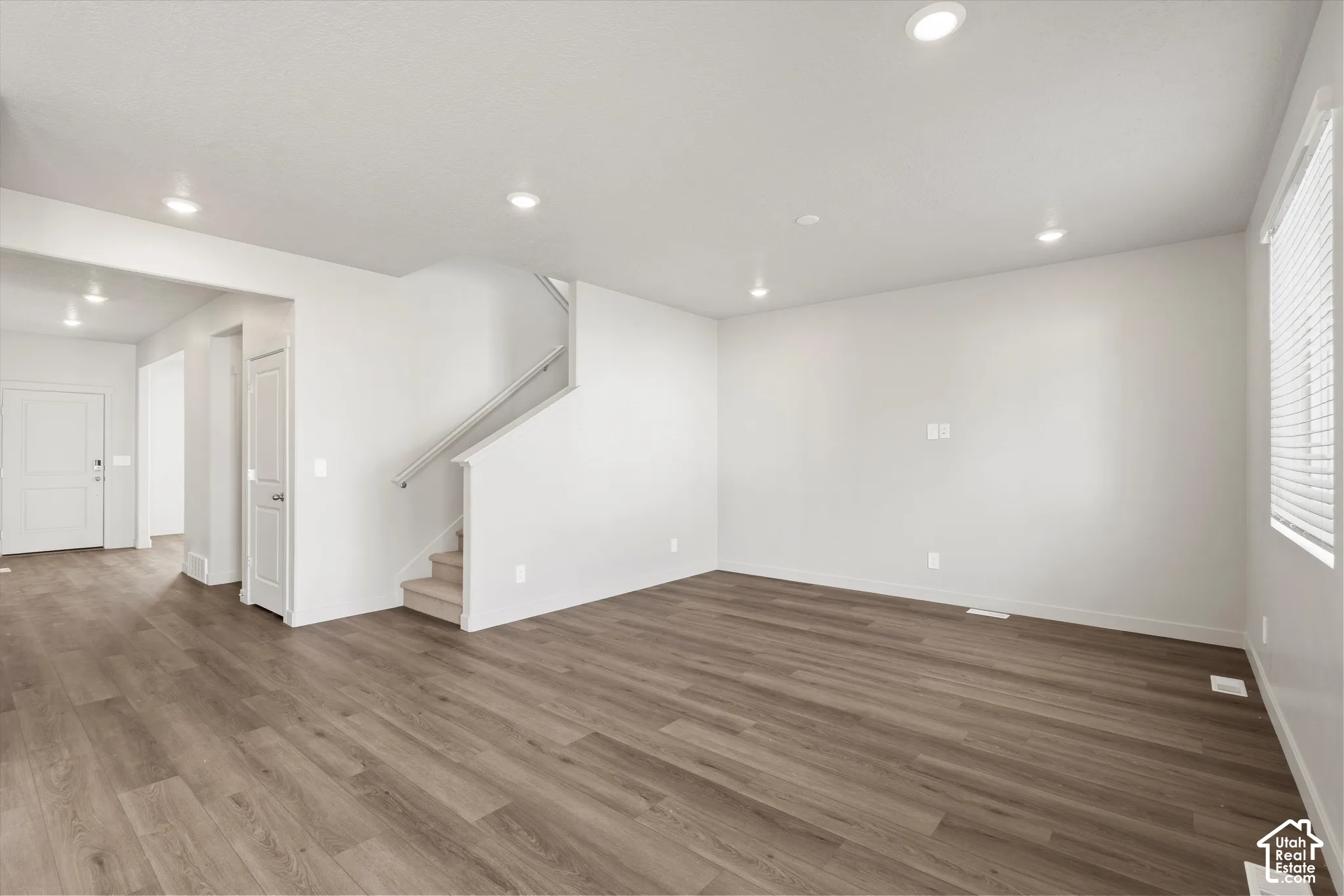 *DISCLAIMER* Interior color package may vary. Open-concept area featuring wood-finish flooring, recessed lighting, neutral wall tones, and a staircase with a white railing