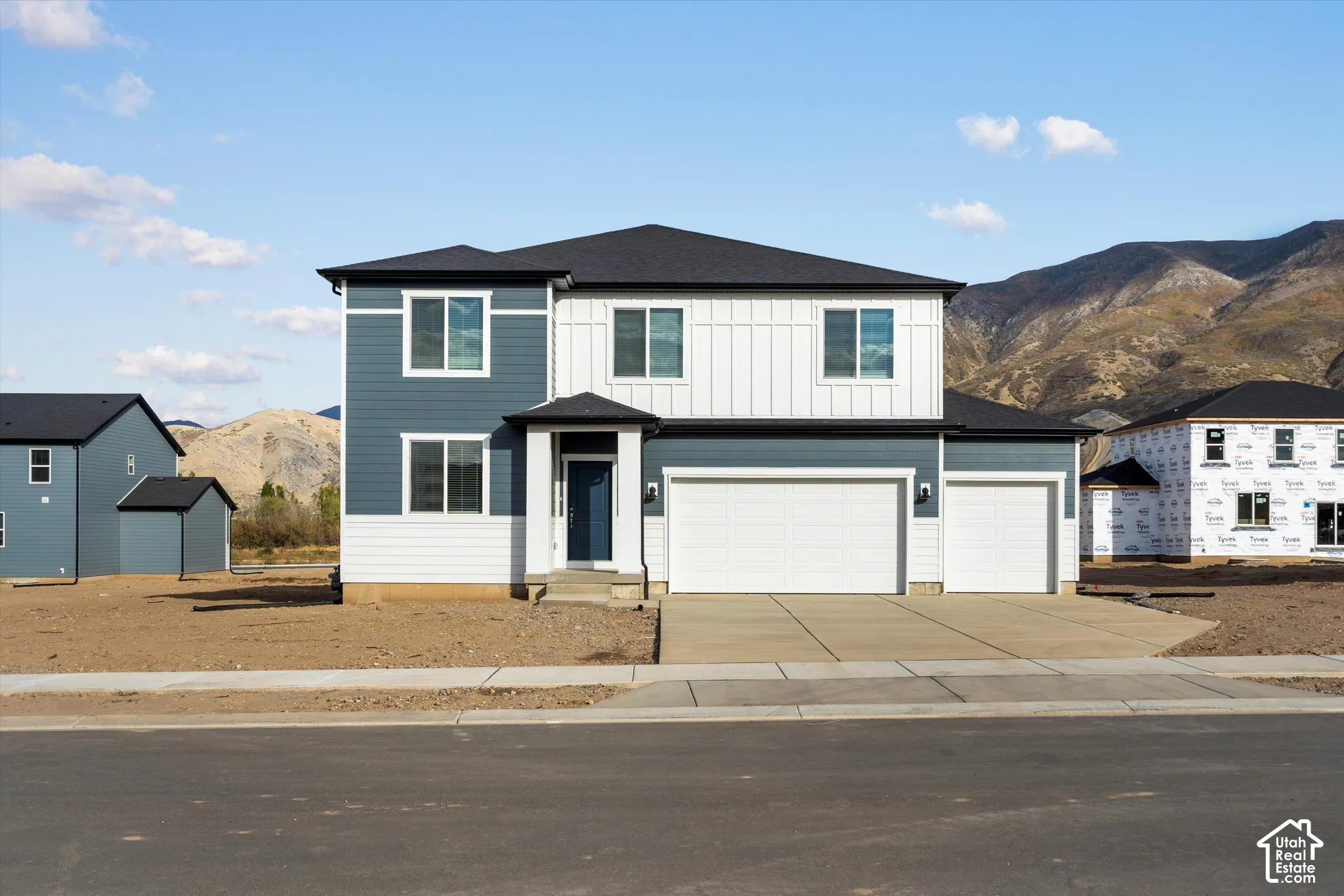 **DISCLAIMER** Elevation and exterior colors may vary. Two-story exterior featuring blue and white horizontal and vertical siding, a three-car garage, concrete driveway, and mountain backdrop