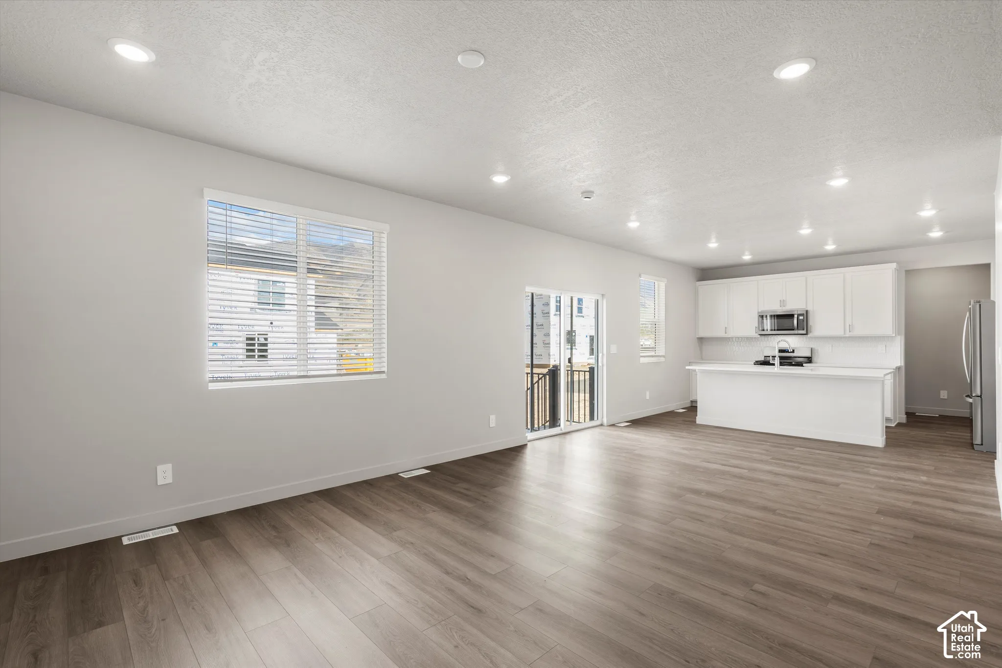 *DISCLAIMER* Interior color package may vary. Open-concept living space featuring wood-finish flooring, recessed lighting, white cabinetry, a center island with countertop seating, and sliding glass doors