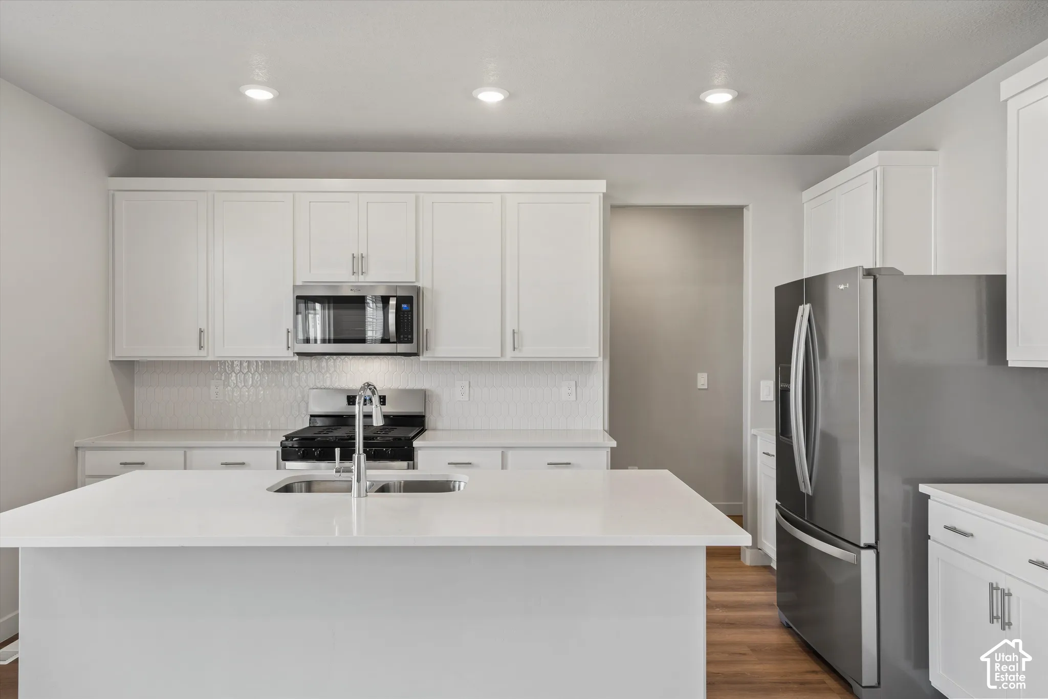 *DISCLAIMER* Interior color package may vary. Kitchen featuring white cabinetry, a center island with a stone-surface countertop, stainless steel appliances, recessed ceiling lighting, and wood-finish flooring