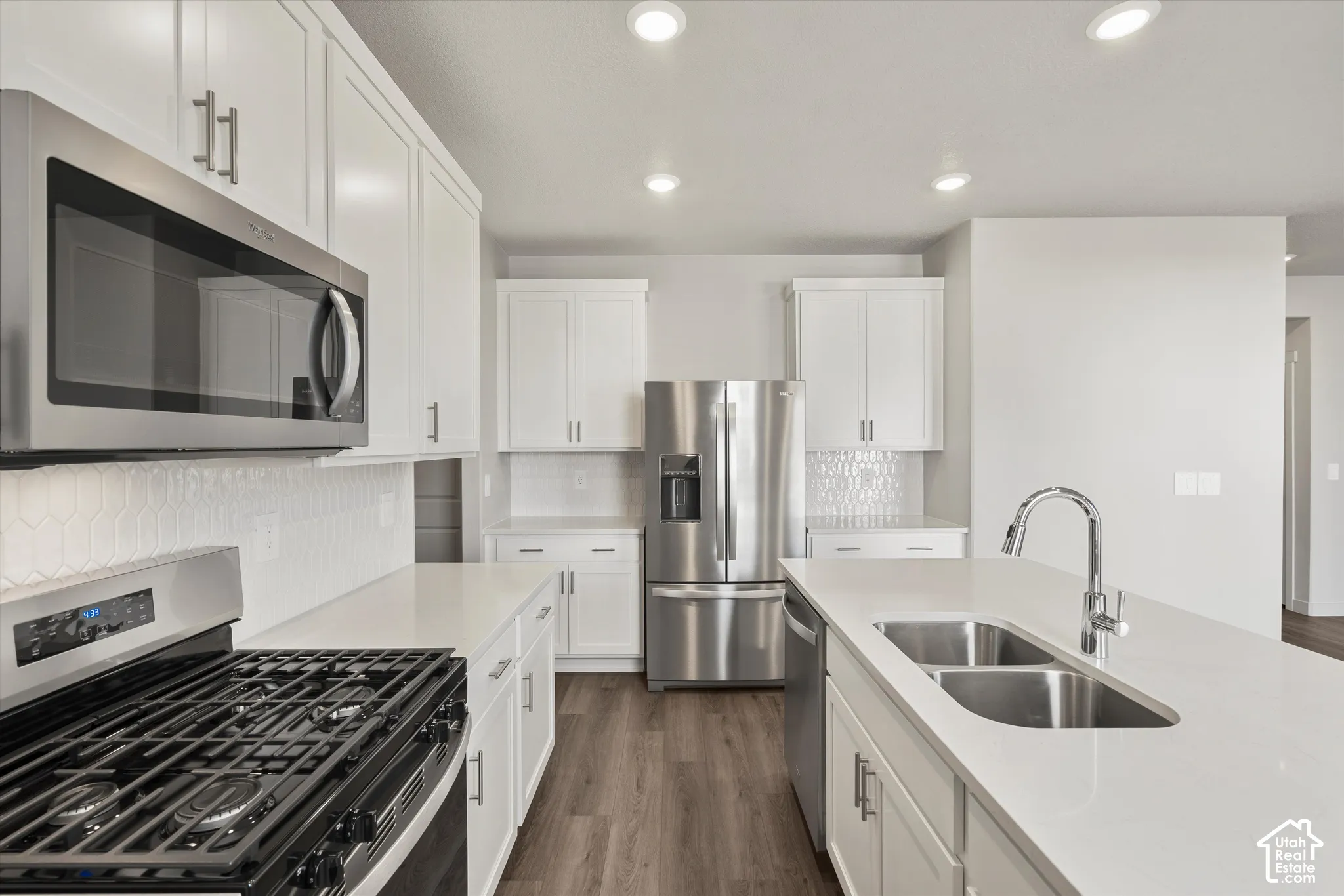 *DISCLAIMER* Interior color package may vary. Kitchen featuring white shaker-style cabinetry, stainless steel appliances, quartz countertops, a central island with an undermount double-basin sink, and recessed lighting