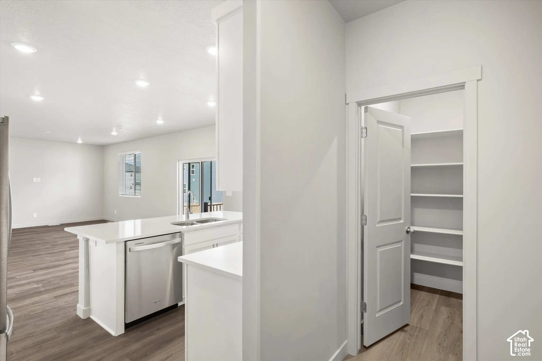 *DISCLAIMER* Interior color package may vary. Kitchen featuring white cabinetry, solid-surface countertops, stainless steel dishwasher, recessed lighting, and a pantry with built-in shelving