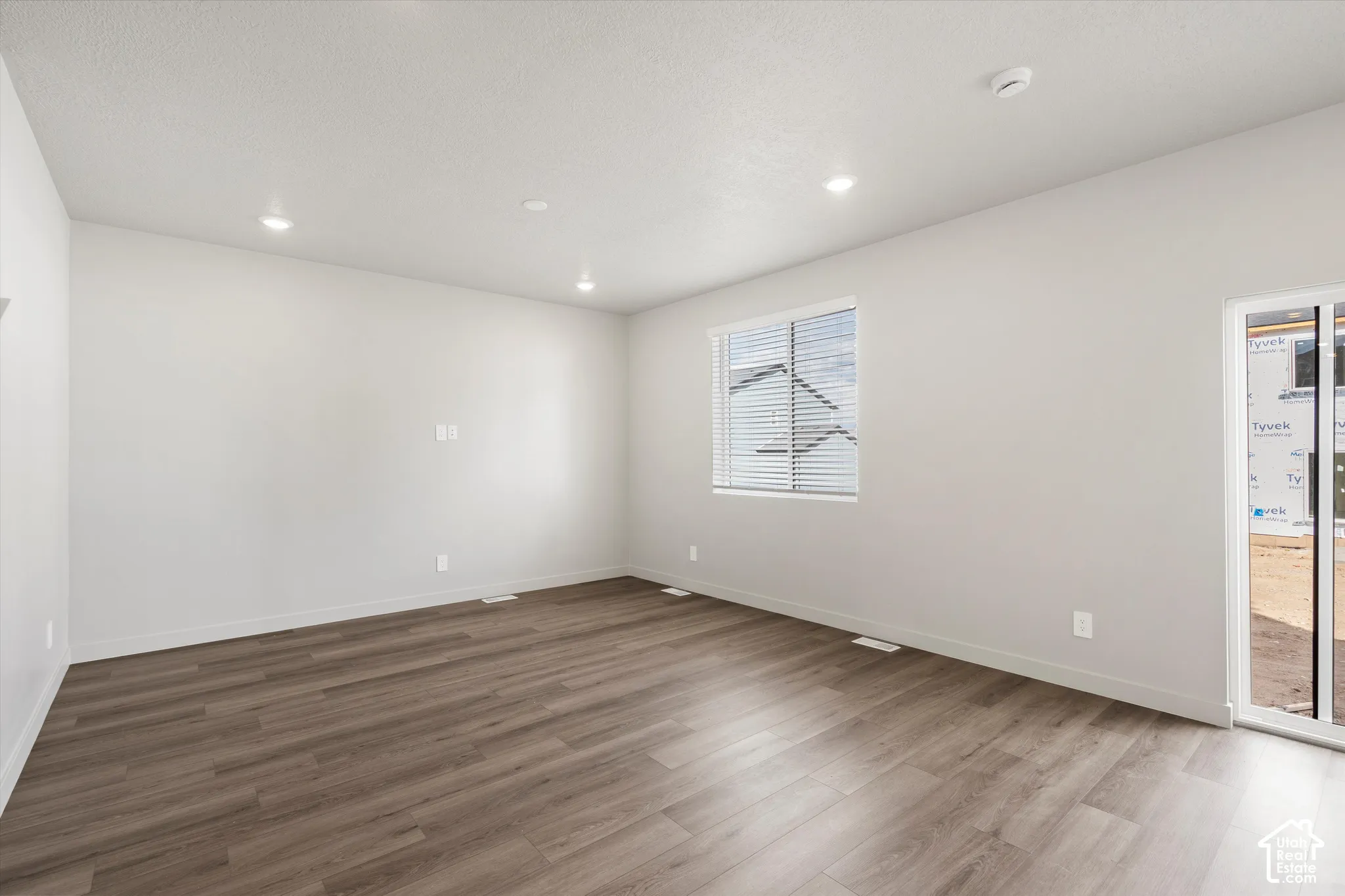 *DISCLAIMER* Interior color package may vary. Interior space featuring wood-finish flooring, neutral wall paint, recessed lighting, a single window with blinds, and a sliding glass door