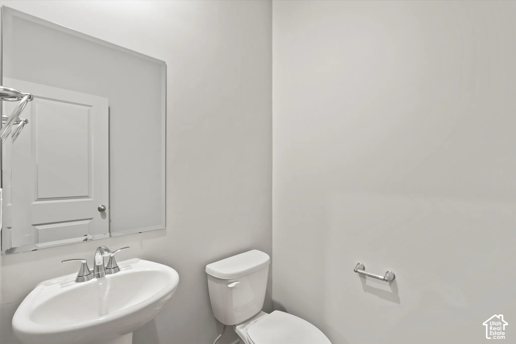 Pedestal sink featuring a dual-handle chrome faucet, wall-mounted mirror, and chrome hardware
