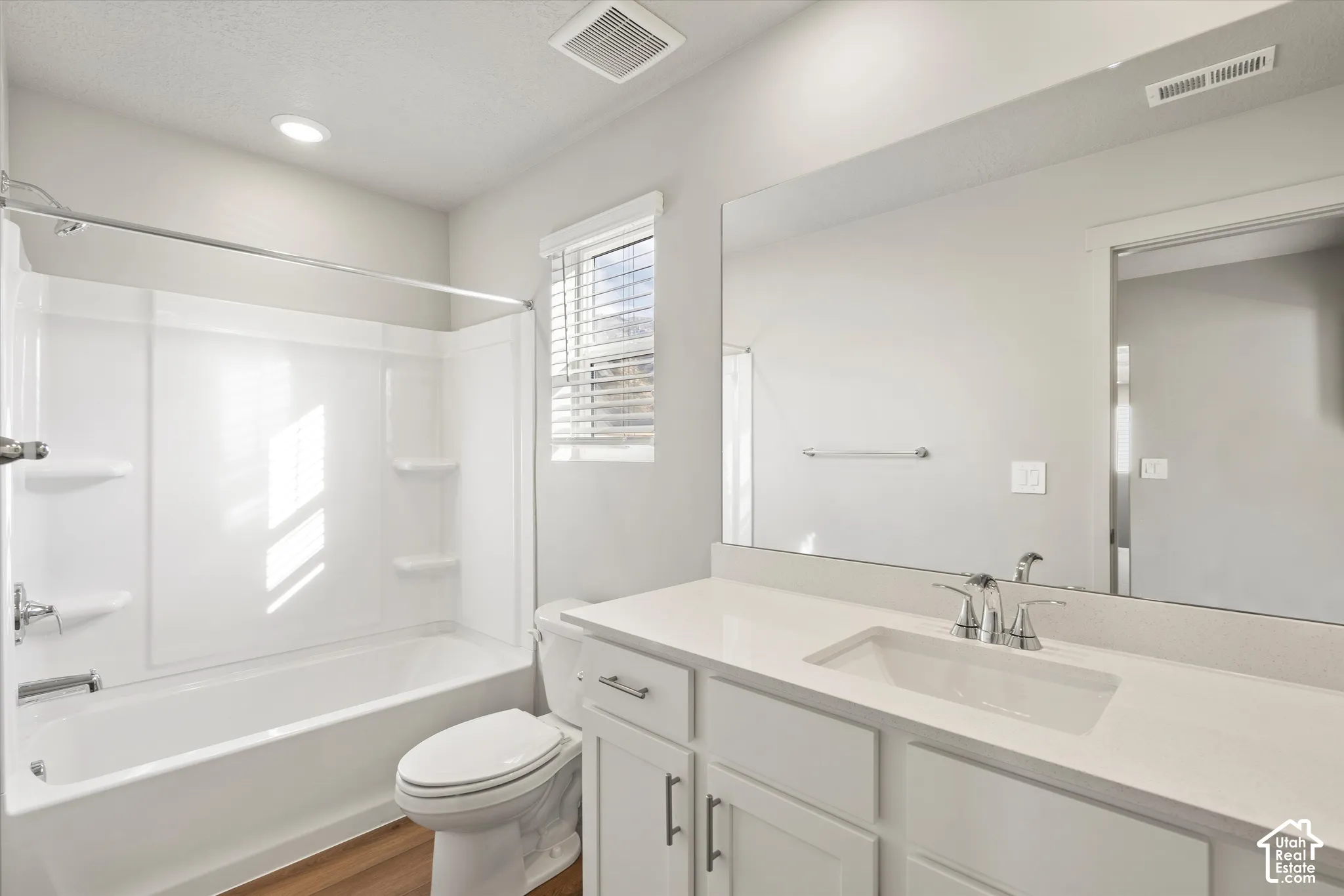 White cabinetry with chrome hardware, countertop with integrated sink, full-width vanity mirror, and tub-shower combination with surround