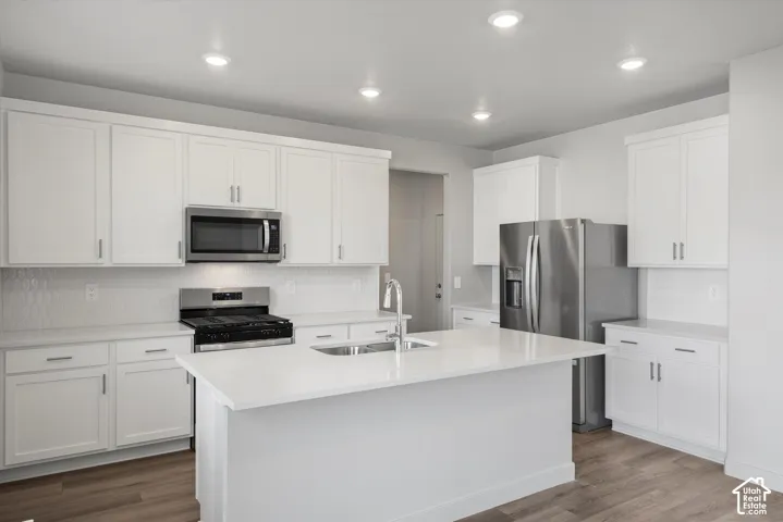 *DISCLAIMER* Interior color package may vary. Kitchen featuring white cabinetry, quartz countertops, a central island with a stainless steel undermount sink, recessed lighting, and wood-finish flooring