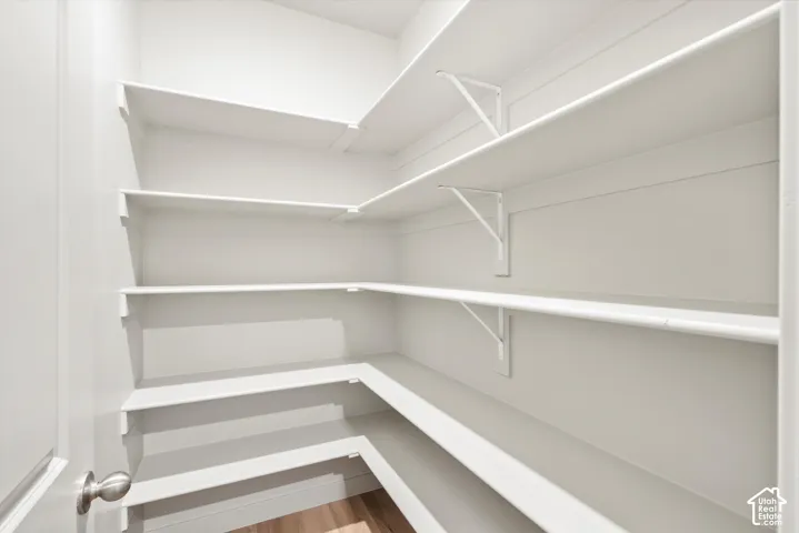 Walk-in storage space featuring multi-tiered shelving, white wall finishes, and wood-finish flooring