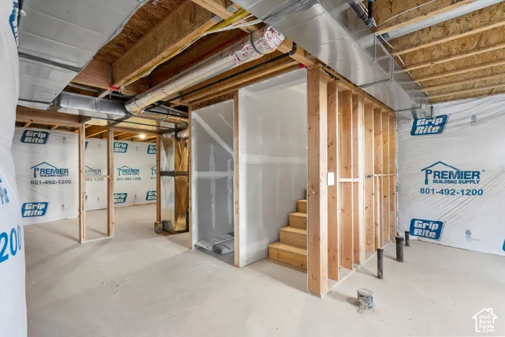 Unfinished basement featuring exposed wood framing, concrete flooring, interior staircase, and exposed HVAC ductwork