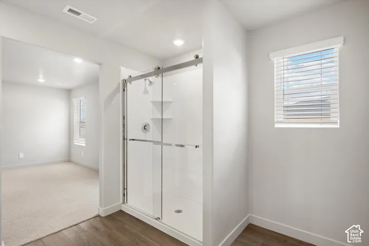 *DISCLAIMER* Interior color package may vary. Walk-in shower featuring a sliding glass enclosure, integrated shelving, and polished chrome hardware, complemented by wood-finish flooring and a window with blinds