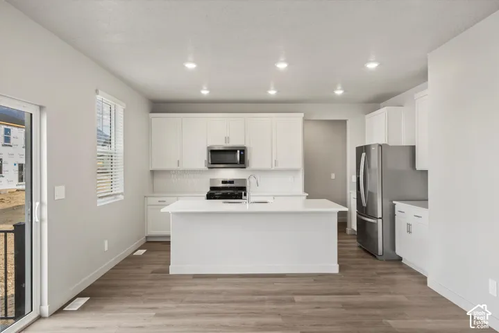 *DISCLAIMER* Interior color package may vary. Kitchen featuring white cabinetry, a center island with a stone-finish countertop, stainless steel appliances, and wood-finish flooring