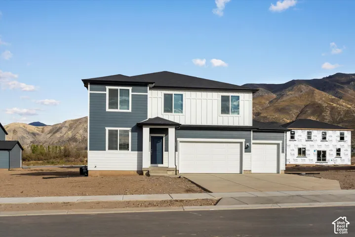 **DISCLAIMER** Elevation and exterior colors may vary. Two-story residence featuring blue horizontal siding, vertical board-and-batten white siding, a three-car garage, and mountain backdrop