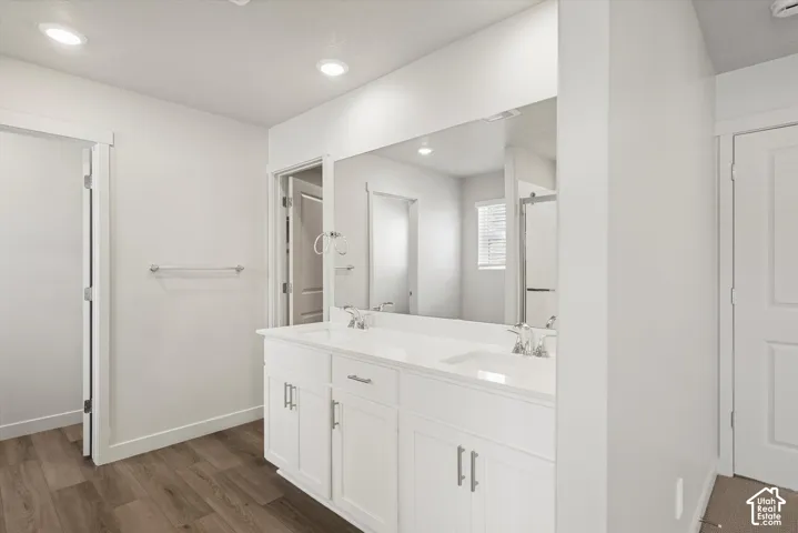*DISCLAIMER* Interior color package may vary. Dual-sink vanity with white cabinetry, light-toned countertop, and chrome faucets, complemented by a large wall-mounted mirror, recessed lighting, and wood-finish flooring