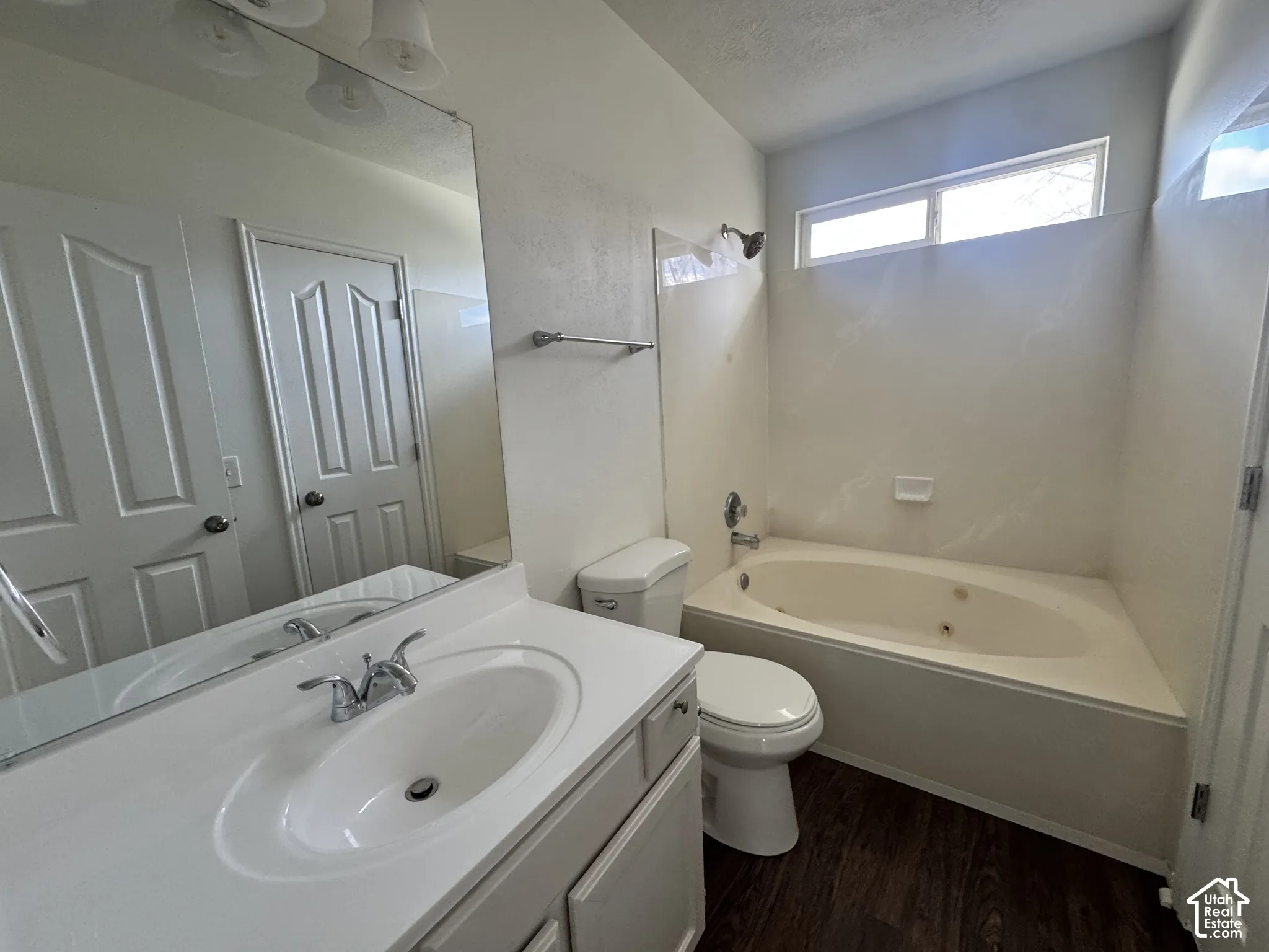 Bathroom featuring a built-in jetted tub, wood-finish flooring, an expansive wall-mounted vanity mirror, and a clerestory window