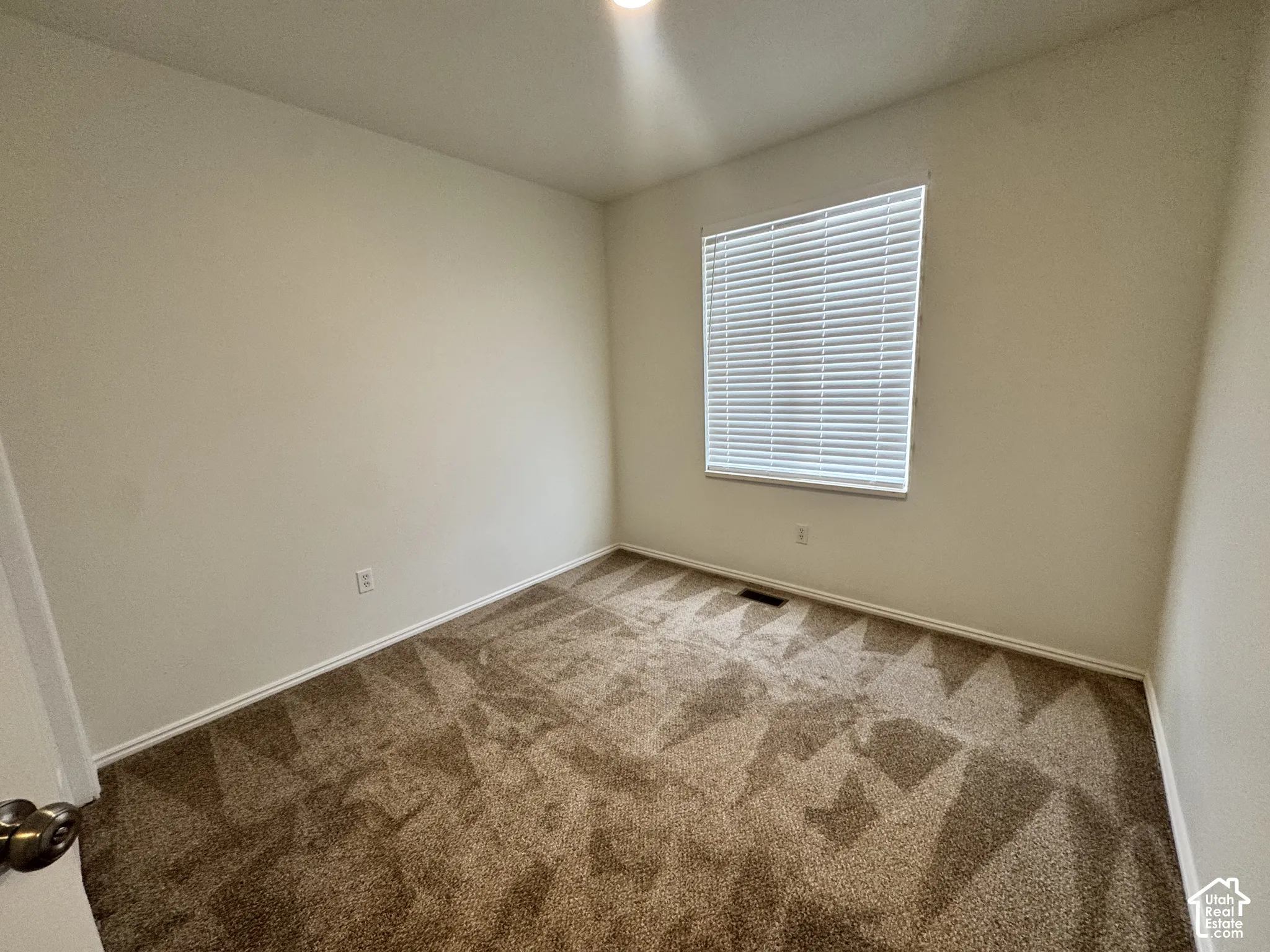 Neutral-toned wall paint, plush carpeting, and a window fitted with horizontal blinds