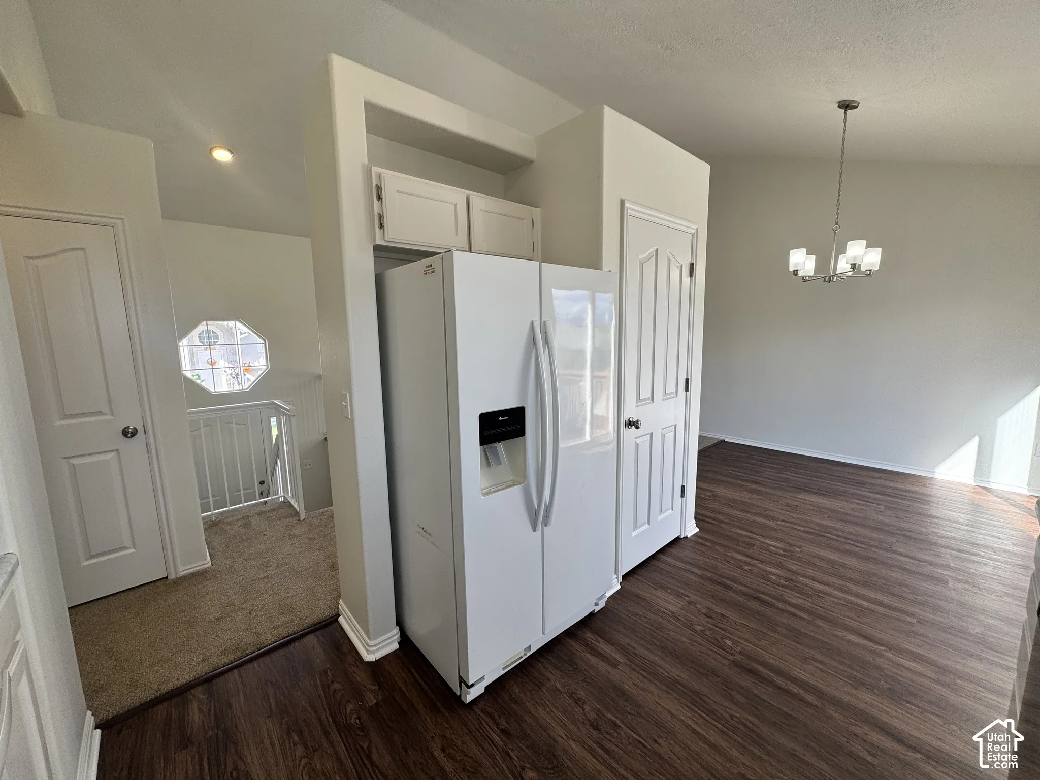 Wood-finish flooring, vaulted ceilings, multi-arm chandelier, built-in cabinetry above the refrigerator space, and an octagonal window accenting the staircase