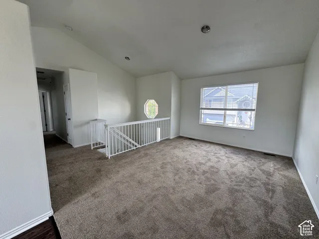 Vaulted ceilings, neutral carpeting, white metal staircase railing, recessed lighting, and a prominent octagon-shaped accent window