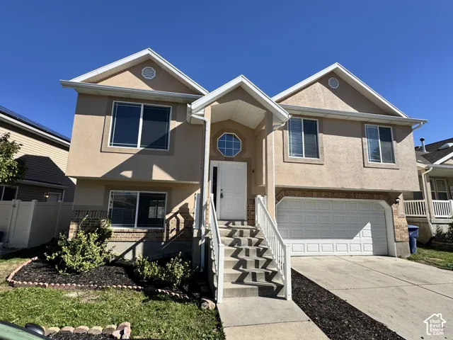 Two-story residence featuring a stucco facade, double-gable roofline, octagonal accent window, concrete driveway, and attached two-car garage