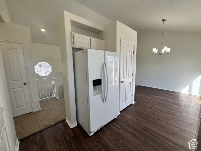 Wood-finish flooring, vaulted ceilings, multi-arm chandelier, built-in cabinetry above the refrigerator space, and an octagonal window accenting the staircase