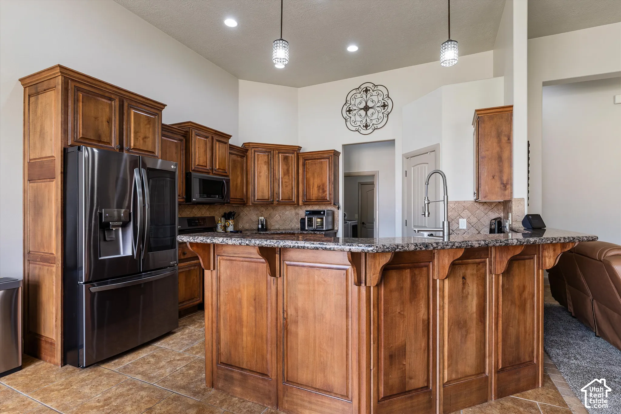 Kitchen featuring stained wood cabinetry, stone-finish countertops, tiled flooring, recessed lighting, and a tiered breakfast bar with a stainless steel faucet