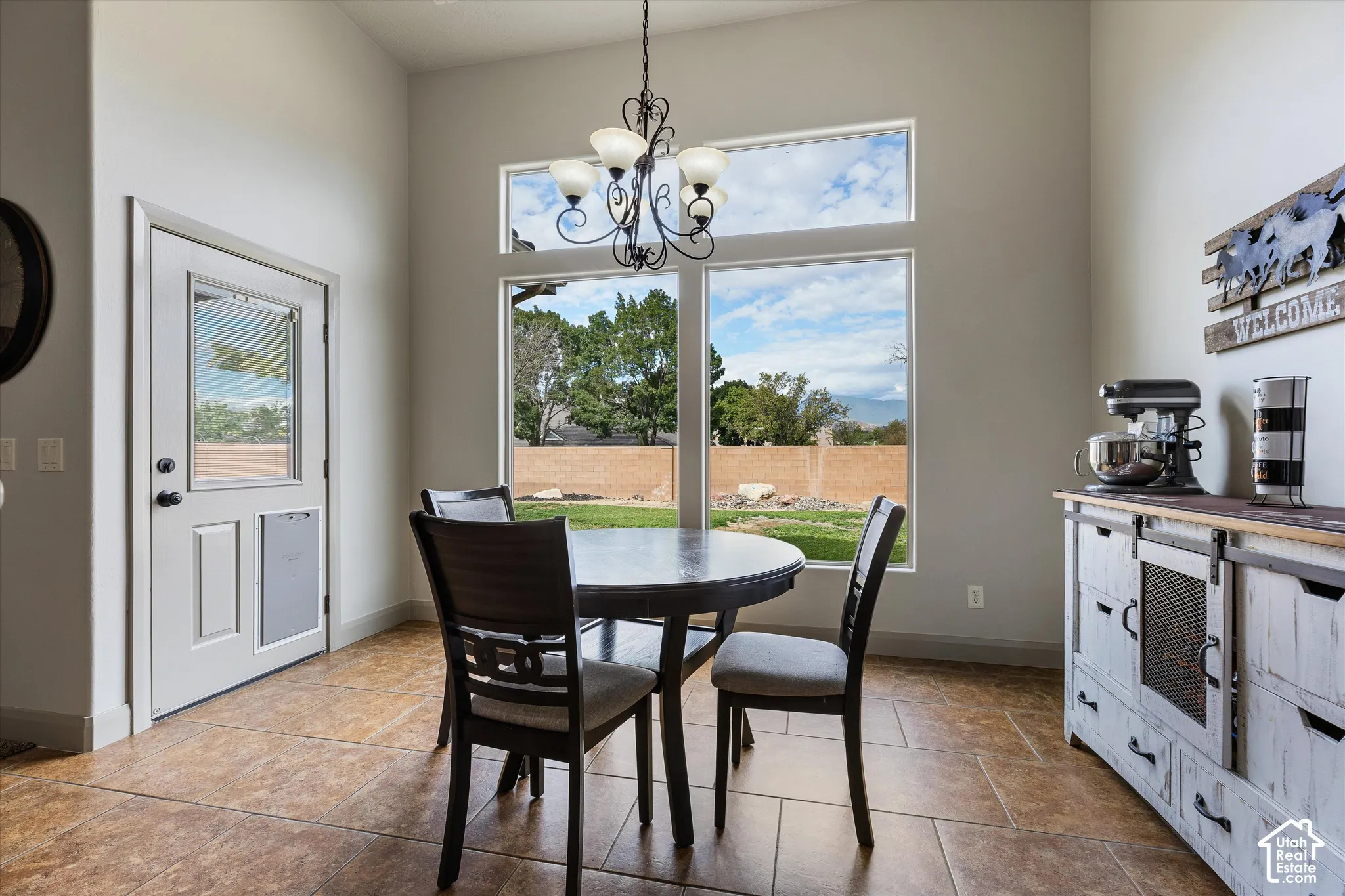 Vaulted ceilings with large windows, decorative iron chandelier, and tile flooring
