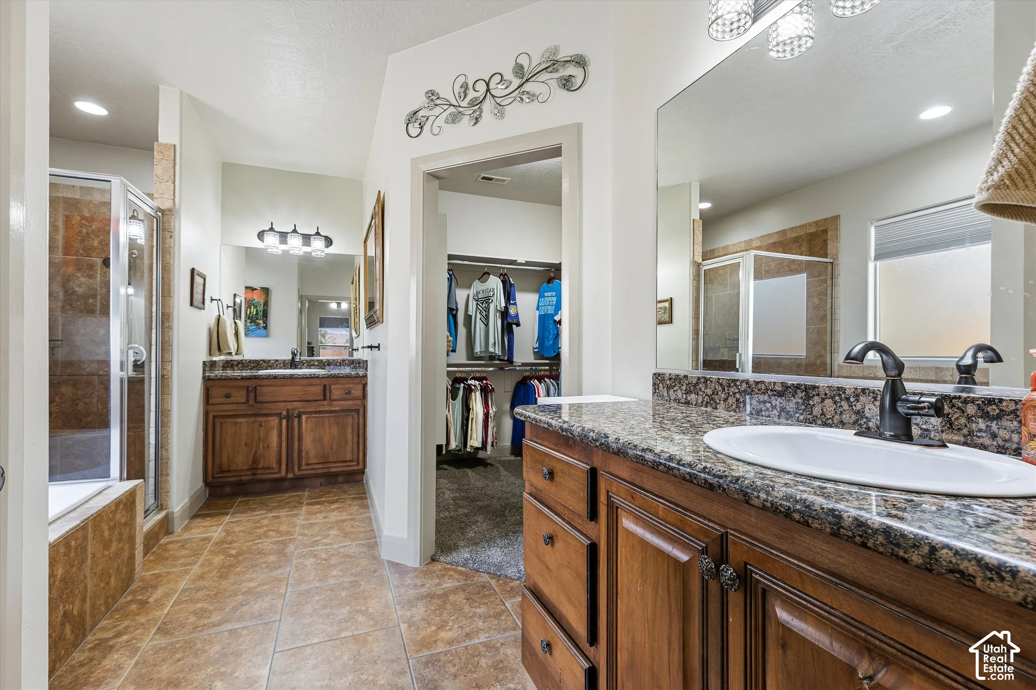 Dual wood-finish vanities with stone-look countertops, drop-in sinks, tile flooring, and a glass-enclosed shower stall