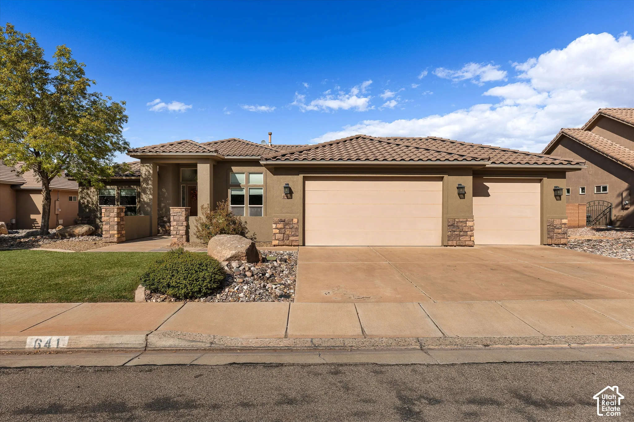 Single-story exterior featuring a tile roof, stone veneer accents, three-car garage, and xeriscaped front yard