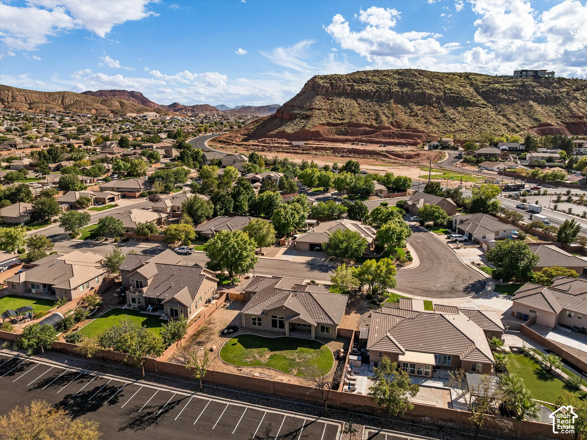 Aerial perspective of a residential neighborhood featuring single-story dwellings with tile roofs, manicured lawns, enclosed rear yards, and prominent mountain backdrops