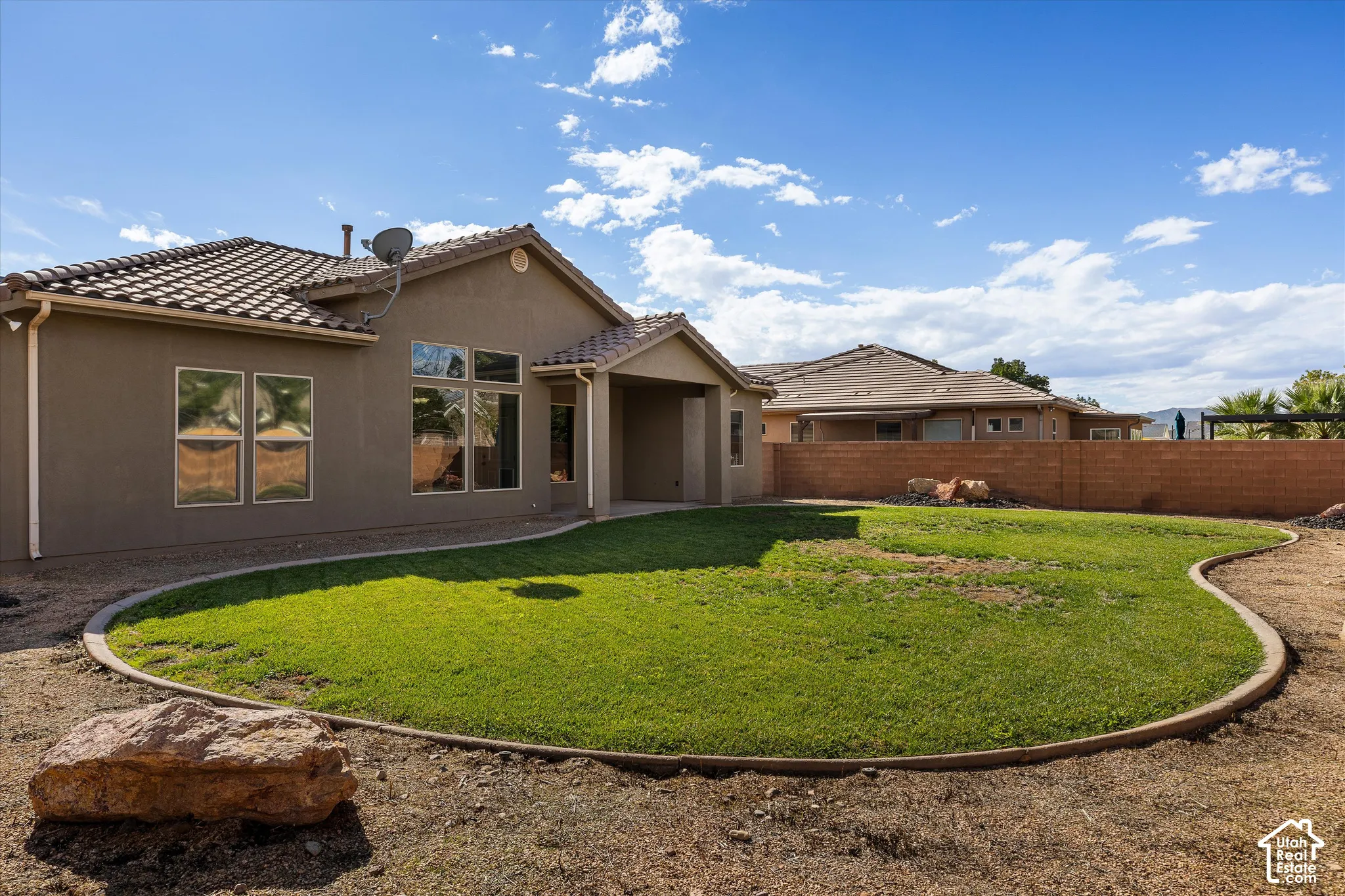 Rear exterior featuring a stucco facade, covered patio, tile roof, and a landscaped backyard with a manicured lawn and concrete curbing