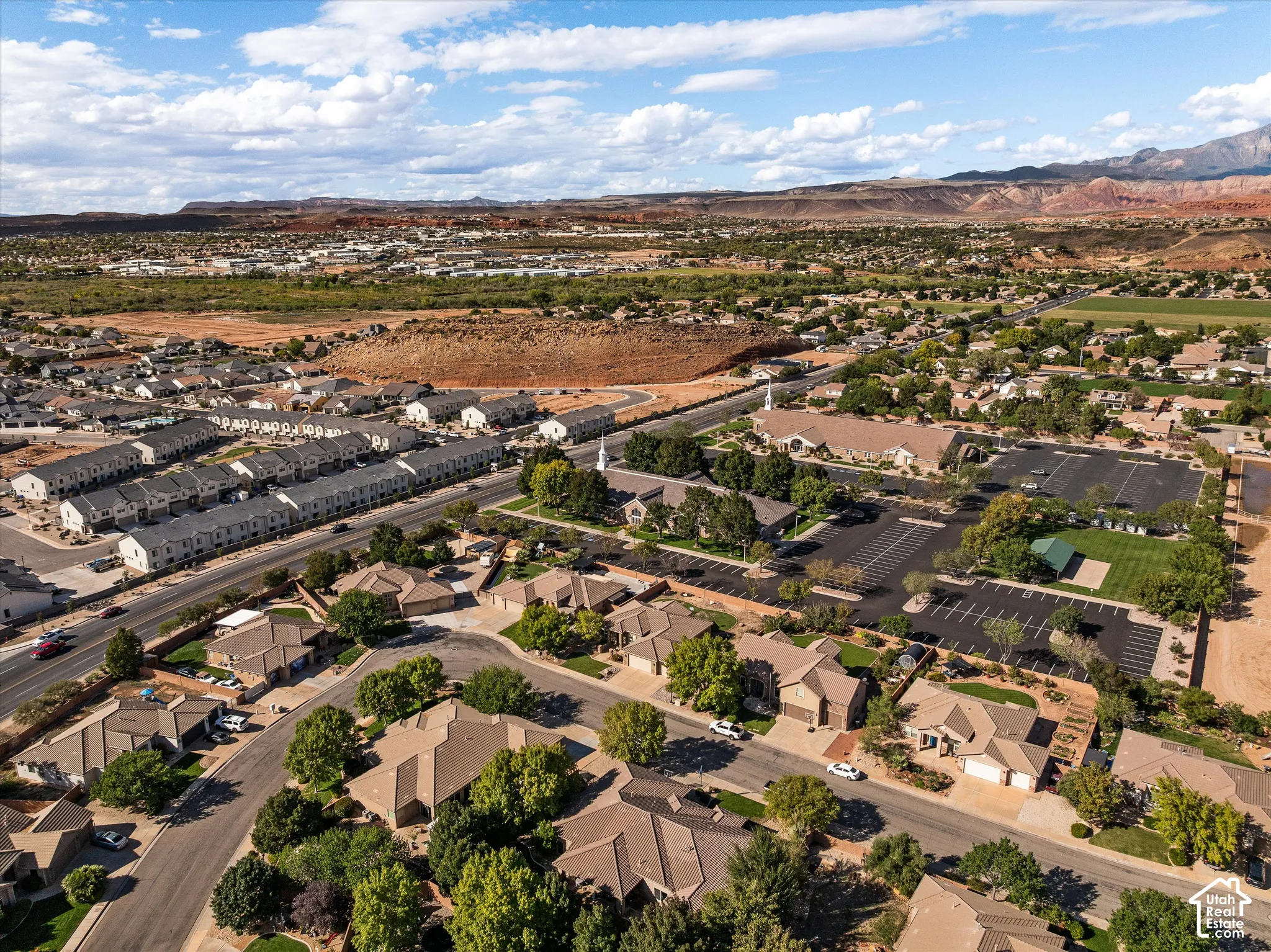 Aerial perspective of a residential neighborhood featuring asphalt paved streets, mature shade trees, single-story residential architecture, and a desert landscape backdrop