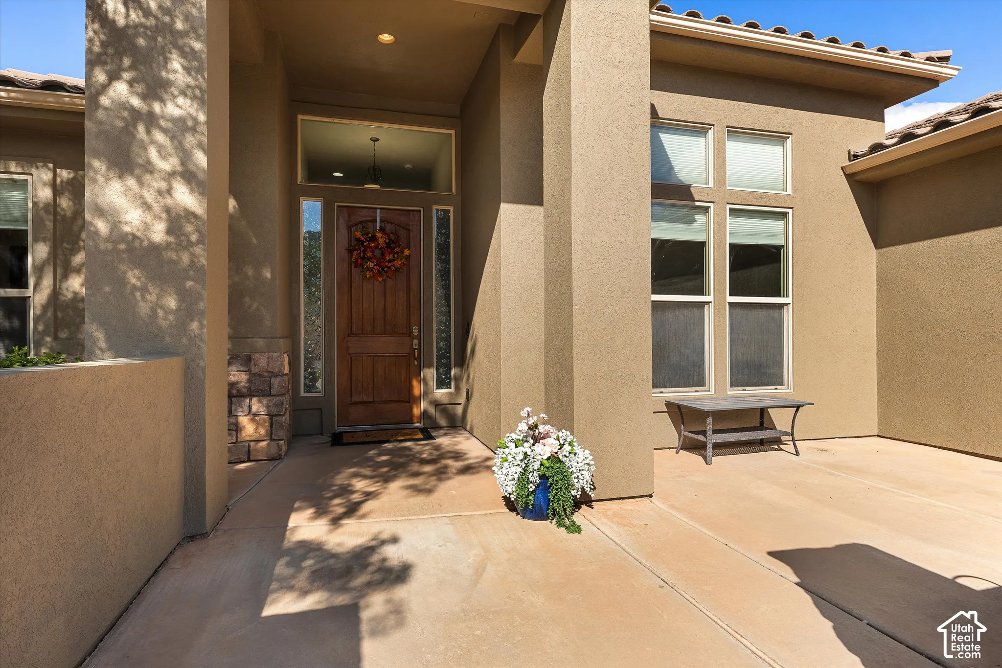 Stucco exterior entry featuring a stained wood front door, decorative stone veneer accent, transom window, and concrete patio
