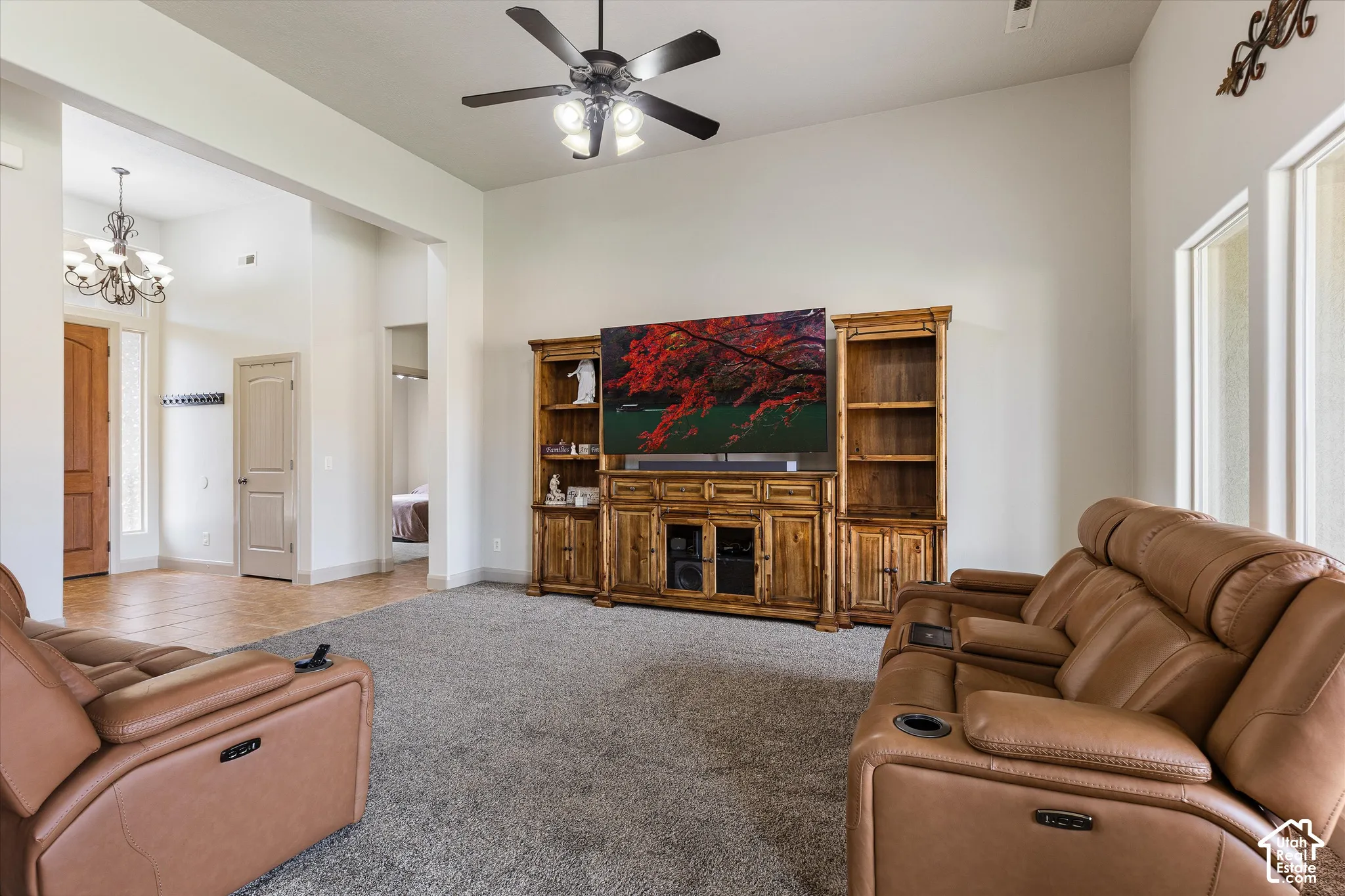 High-ceiling living area featuring neutral wall tones, carpeted flooring, a ceiling fan with integrated lighting, and built-in wood cabinetry