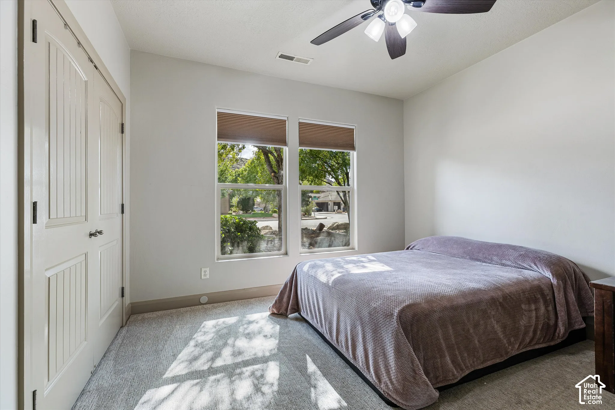 Neutral-toned interior featuring dual-pane windows with integrated blinds, wall-to-wall carpeting, a ceiling fan with integrated lighting, and a double-door closet