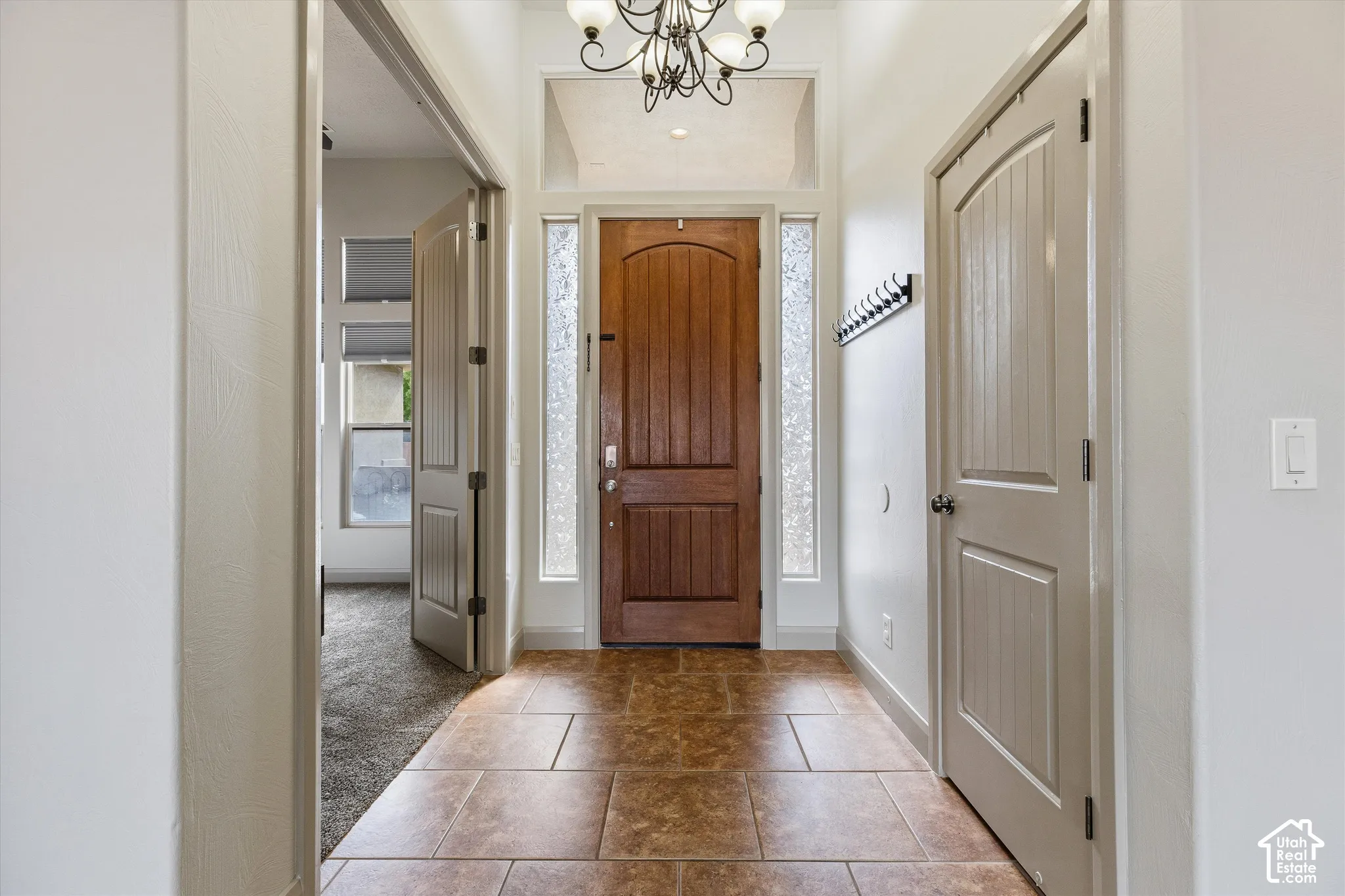 Entryway featuring stone-finish tile flooring, a solid wood arched-top entry door, sidelights with textured glass, an overhead chandelier, and interior three-panel doors