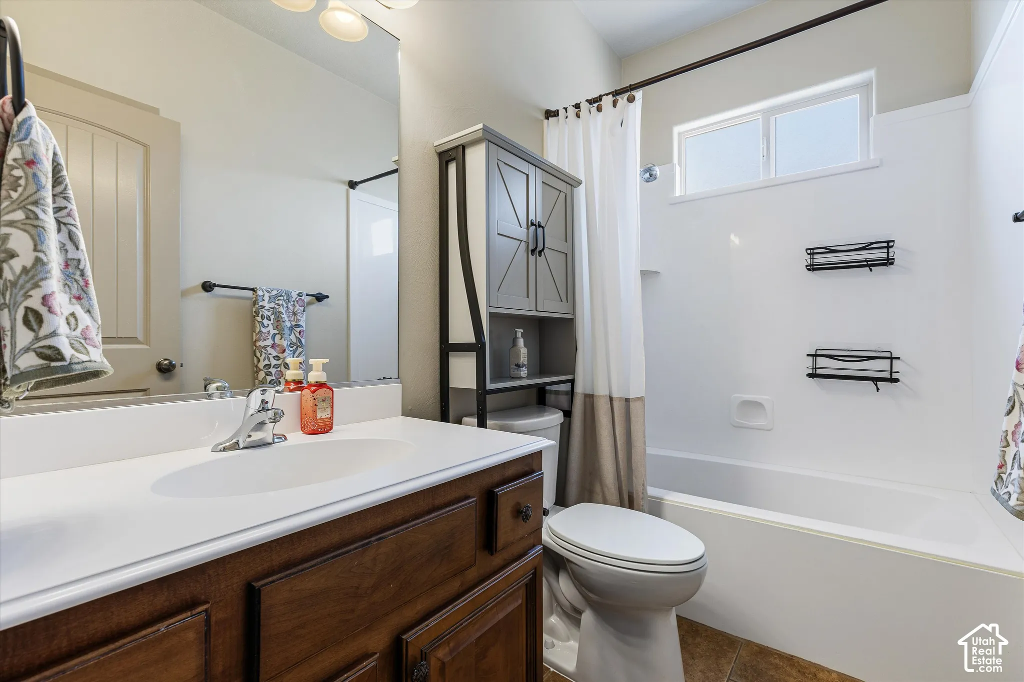 Bathroom featuring a wood-finish vanity with a white countertop and oval undermount sink, large wall-mounted mirror, and a tub-shower combination with a white surround