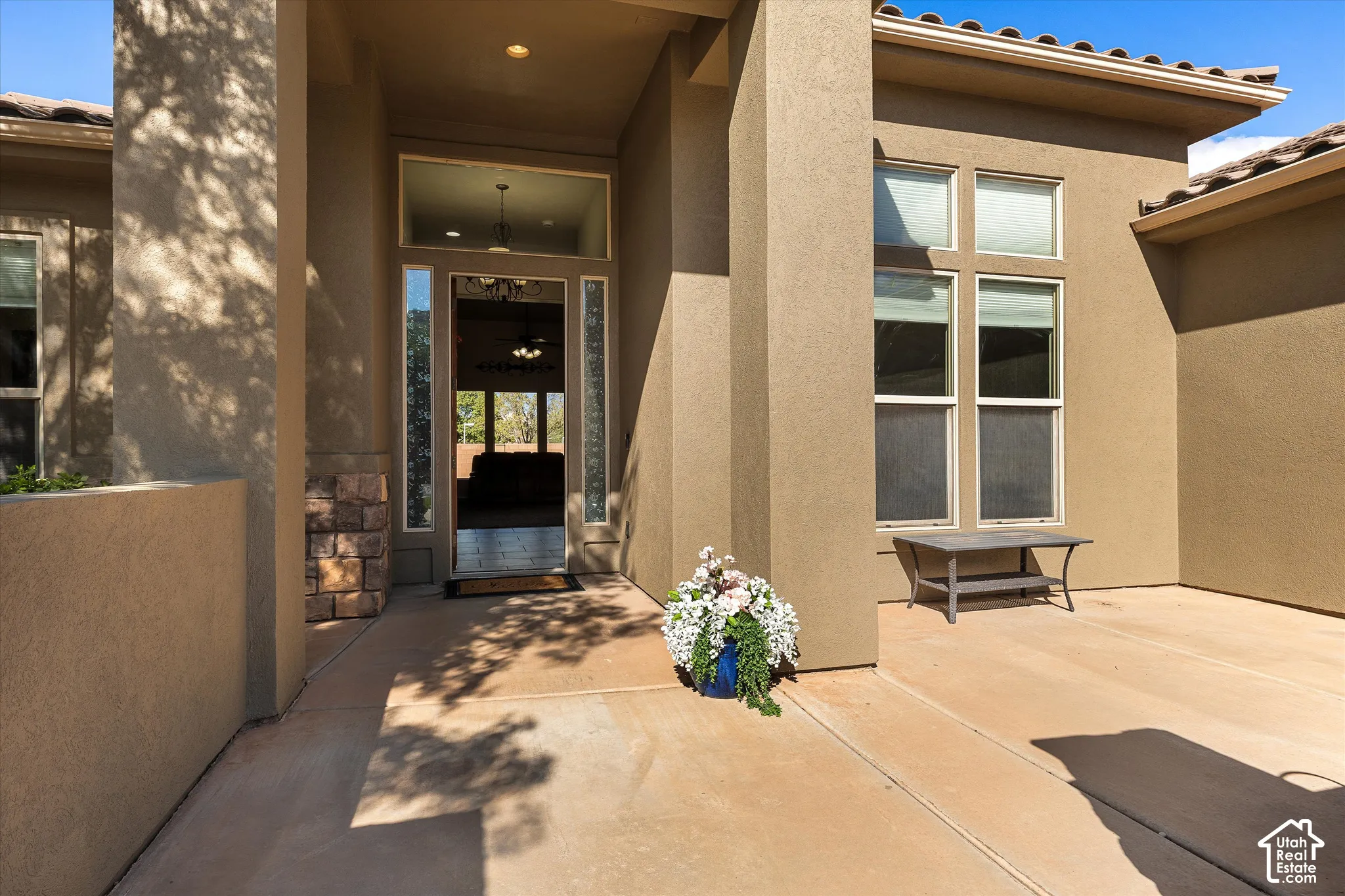 Stucco facade entrance featuring a covered patio, tile roof, masonry stone detailing, and multi-pane transom windows