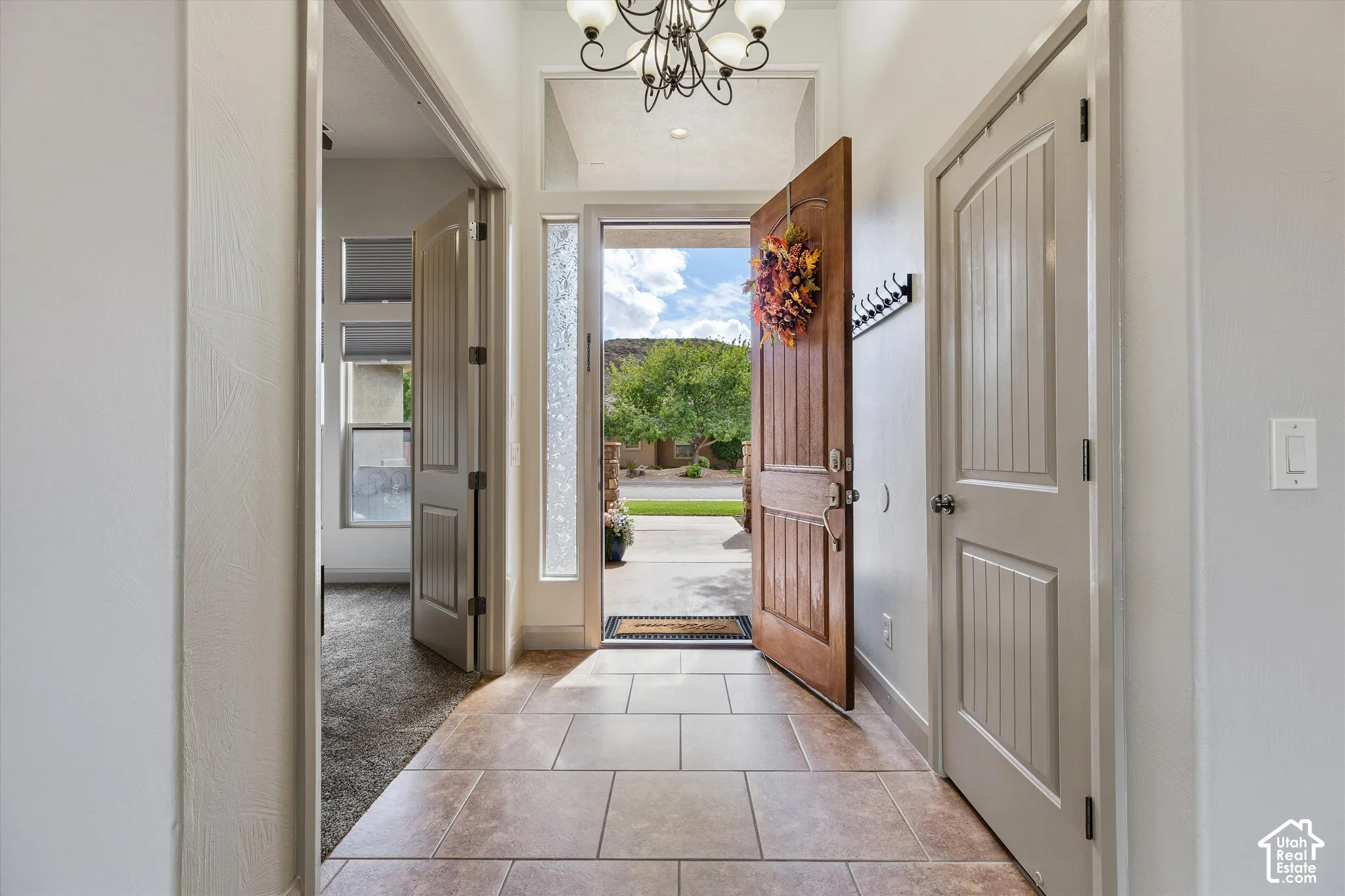 Entryway featuring tile flooring, a wood-grain paneled front door, a decorative multi-bulb chandelier, a textured glass sidelight, and arched-top interior doors