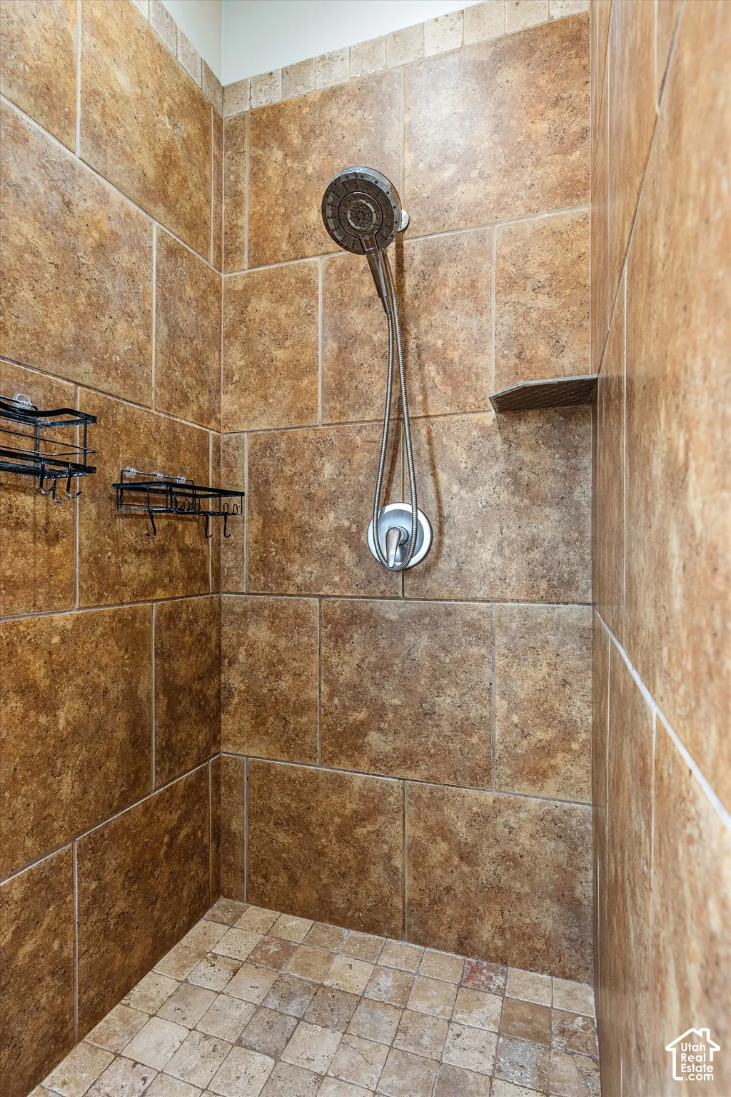 Shower enclosure featuring large-format stone wall tile, mosaic tile flooring, a chrome handheld shower head with single-handle mixing valve, and a built-in stone corner shelf
