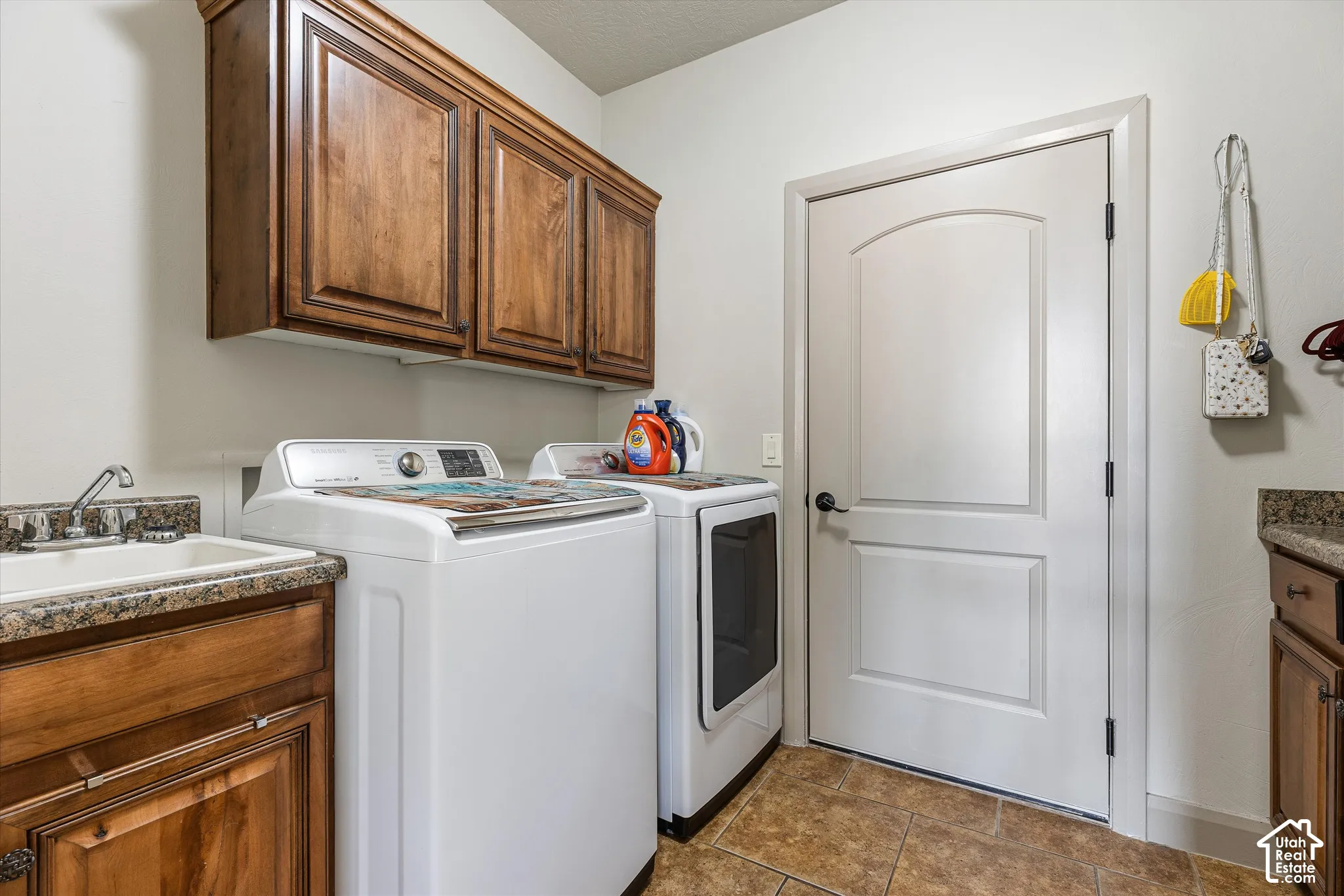 Utility area featuring wood-finish cabinetry, stone-texture countertops, tile flooring, and a drop-in sink with a chrome faucet