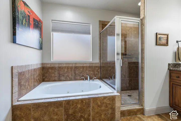 Bathroom featuring a jetted soaking tub, tiled surround, glass-enclosed shower, and built-in cabinetry