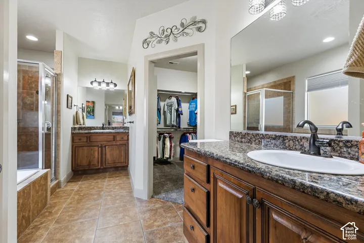 Dual wood-finish vanities with stone-look countertops, drop-in sinks, tile flooring, and a glass-enclosed shower stall