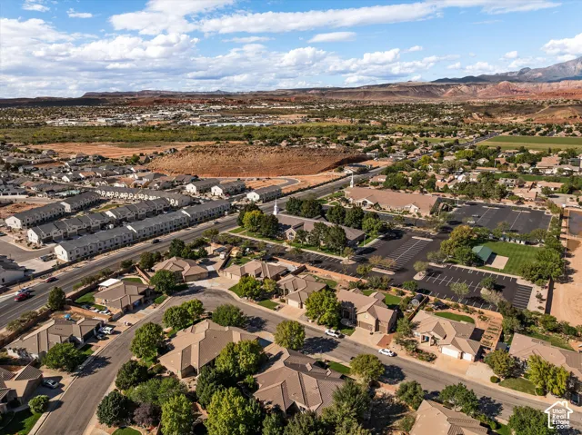 Aerial perspective of a residential neighborhood featuring asphalt paved streets, mature shade trees, single-story residential architecture, and a desert landscape backdrop